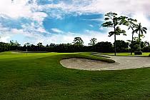 Beautiful golf course with a sand trap, green fairway, and tall trees under a partly cloudy sky at Atlantis CC.