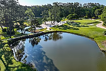 A scenic view of Eagle Nest Golf Club featuring a large pond, lush green fairways, sand bunkers, and tall trees under a clear sky.