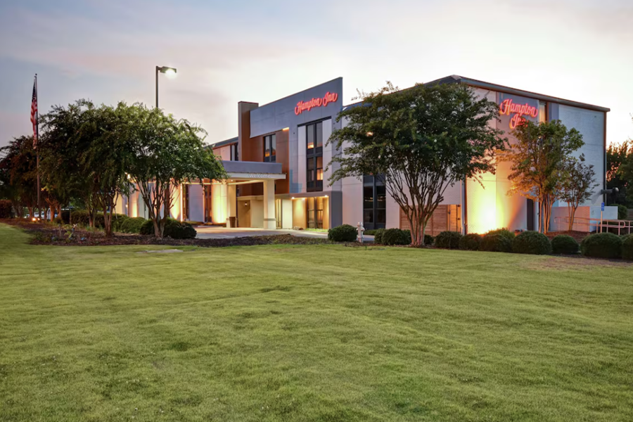 Hampton Inn Auburn exterior with lush lawns and evening lighting, offering stylish accommodation for golf enthusiasts.