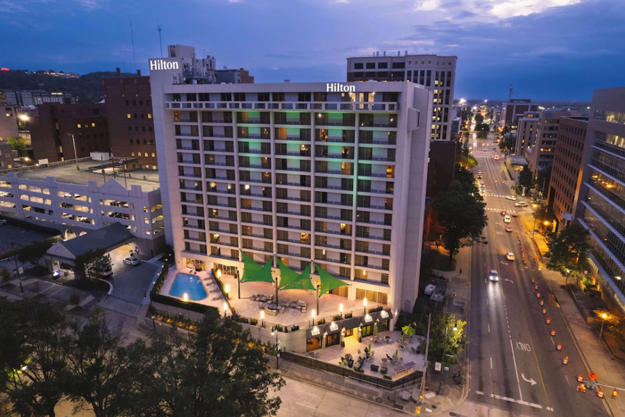 Hilton Birmingham Downtown hotel at dusk, featuring a lit exterior, rooftop pool, and cityscape view, near UAB.