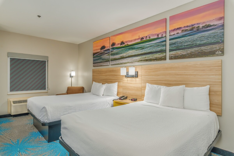 Modern hotel room with two beds, vibrant golf course artwork, beige walls, and blue patterned carpet at Days Inn, Prattville.