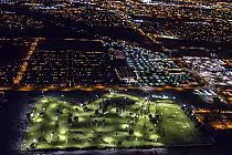 Night view of Indio Golf Course illuminated with bright lights, surrounded by city lights in Palm Springs at night.