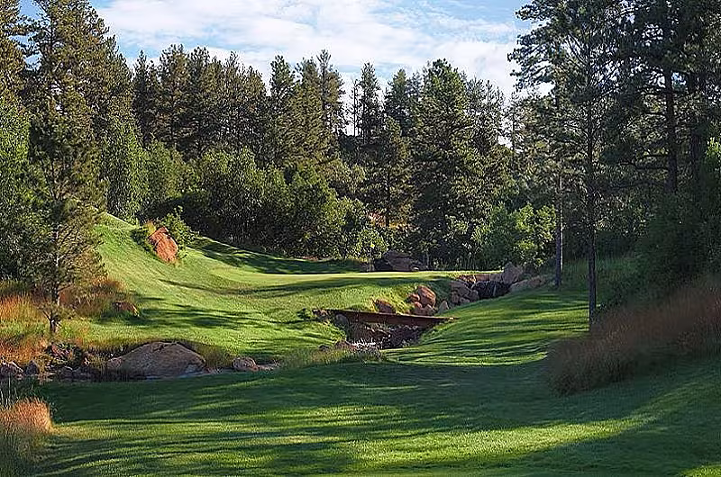 A scenic golf course in Denver, Colorado, with lush green fairways, tall trees, rocks, and a small stream, ideal for top-tier golf and relaxation.