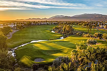 Scenic golf course at sunset with lush green fairways, palm trees, water features, and the San Jacinto Mountains in the background.