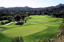 Scenic view of Mt. Woodson Golf Club with lush green fairways, a putting green with flag, surrounded by trees and mountainous landscape.