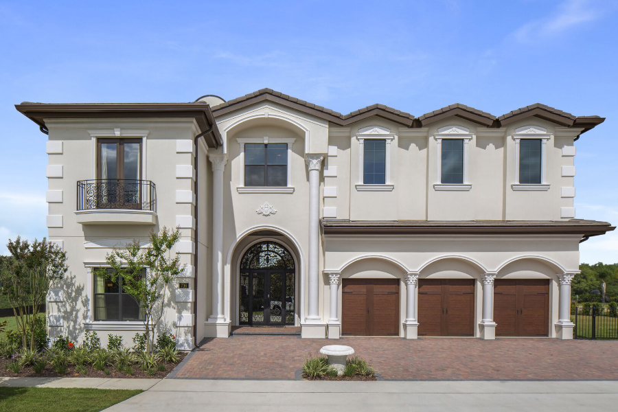 Luxurious 13-bedroom vacation home with elegant cream facade and multiple garage doors, set against a clear blue sky.