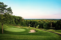 Scenic view of Vespra Hills Golf Club with a green, sand bunkers, trees, and a distant horizon under a clear sky.