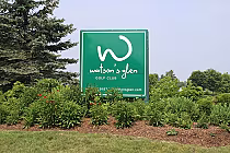 Sign for Watson's Glen Golf Club surrounded by lush green plants and trees in scenic Ontario landscape.