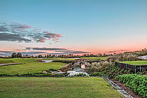 Scenic view of Royal St. Cloud Golf Links with lush green fairways, a small stone bridge over a stream, and a colorful sunset sky.