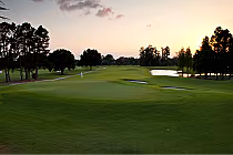 Scenic view of Dubsdread Golf Course in Orlando at sunset, featuring lush green fairways, trees, water hazards, and a flag on the green.