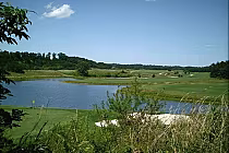 Scenic view of Horse Creek Golf Course with a water hazard, lush green fairways, and rolling hills under a blue sky.