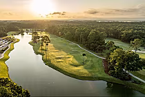 A scenic aerial view of Hilton Head National Golf Club at sunset, featuring a winding waterway, lush green fairways, and trees.
