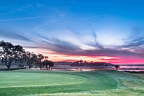 Scenic golf course at sunset with lush green fairway, trees, and a water body near Hilton Head Island, offering a luxurious golf experience.