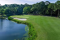 A scenic golf course with a green, sand bunkers, and a water hazard, surrounded by trees at Golden Bear Golf Club in Hilton Head, SC.