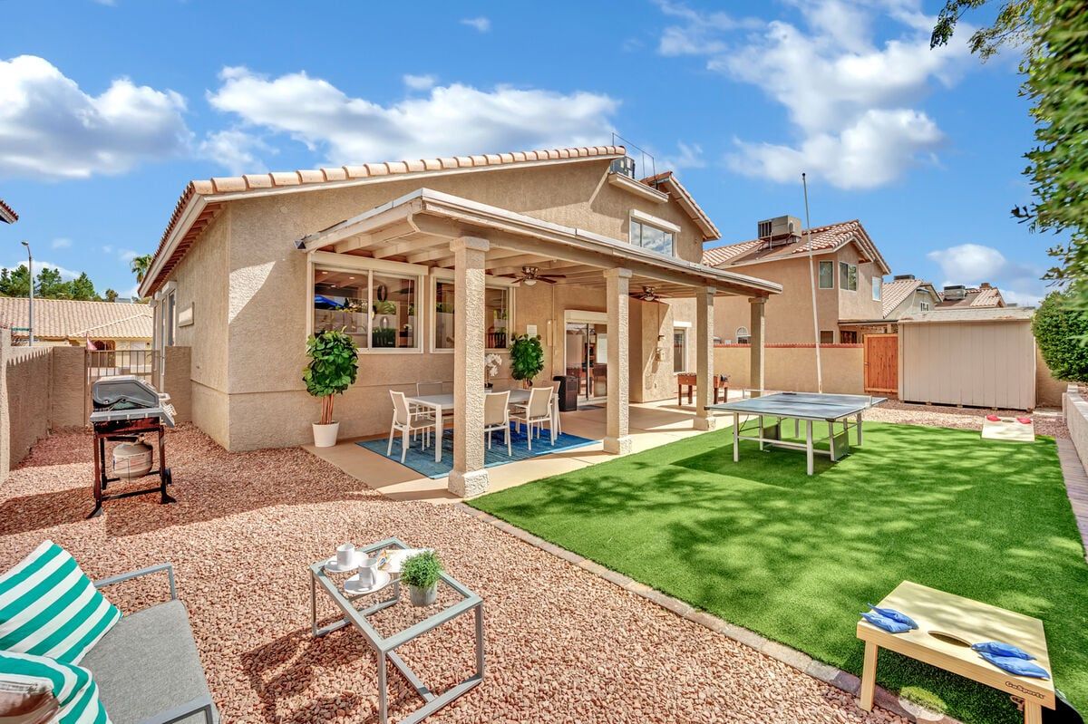 4 Bedroom Rental Home Bright backyard of a 4-bedroom rental home with a covered patio, outdoor dining, ping pong table, and landscaped yard.