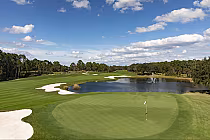 Scenic view of Tranquilo Golf Club at Four Seasons Orlando with a green, sand traps, water hazard, and blue sky with clouds.