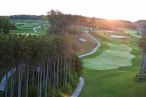 A scenic golf course with lush green fairways, sand traps, and tall trees, bathed in warm sunlight at sunset.