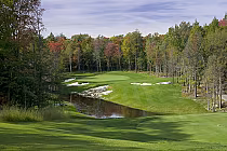 Scenic golf course at Manitou Ridge with lush green fairway, sand bunkers, and a pond, surrounded by autumn trees.
