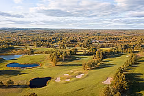 Aerial view of Cedar Green Golf Club showcasing lush green fairways, water hazards, and dense surrounding forests under a cloudy sky.