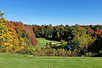 Scenic view of Blue Springs Golf Club with lush green fairways, surrounded by vibrant autumn trees and a small pond.
