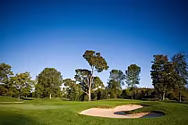 Hidden Lake Golf Club scenic view with lush green fairway, sand bunker, and surrounding trees under a clear blue sky.