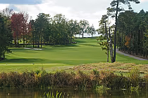 Scenic view of a lush, green golf course at Black Bear Ridge, surrounded by trees under a partially cloudy sky.