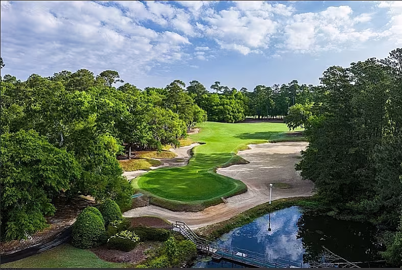 Scenic Myrtle Beach golf course with lush fairways, sand traps, and a pond under a blue sky with scattered clouds.