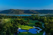 Aviara Resort Golf Club showcases lush green fairways, a serene lake, and surrounding hills under a clear blue sky.