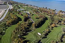 Aerial view of Rochester Place Golf Club with lush fairways, sand traps, and nearby coastal shoreline under clear skies.