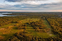 Aerial view of lush green fairways and trees at Monte Vista Golf Club under a partly cloudy sky, with lakes in the distance.