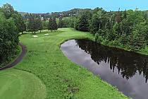 Scenic view of a golf course at Deerhurst Highlands, featuring lush greenery, sand traps, and a reflective pond under clear skies.