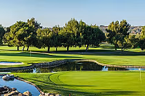 Lush green golf course with a pond and sandy bunker, surrounded by tall trees under a clear blue sky at Temecula Creek Golf Club.