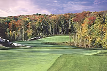Scenic golf course with lush green fairways, surrounded by vibrant autumn trees under a partly cloudy sky.