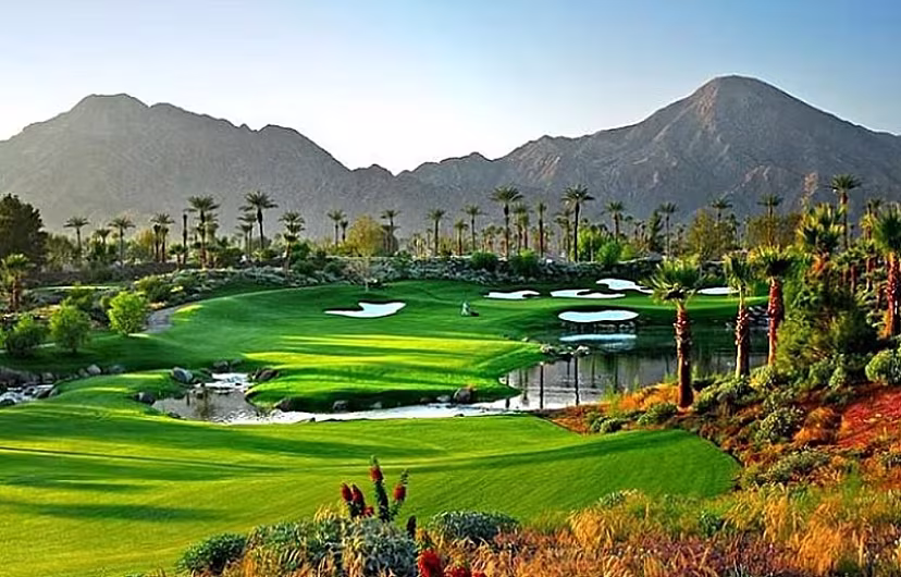 Scenic golf course in Palm Springs with vibrant green fairways, surrounding palm trees, and distant mountains at sunset.