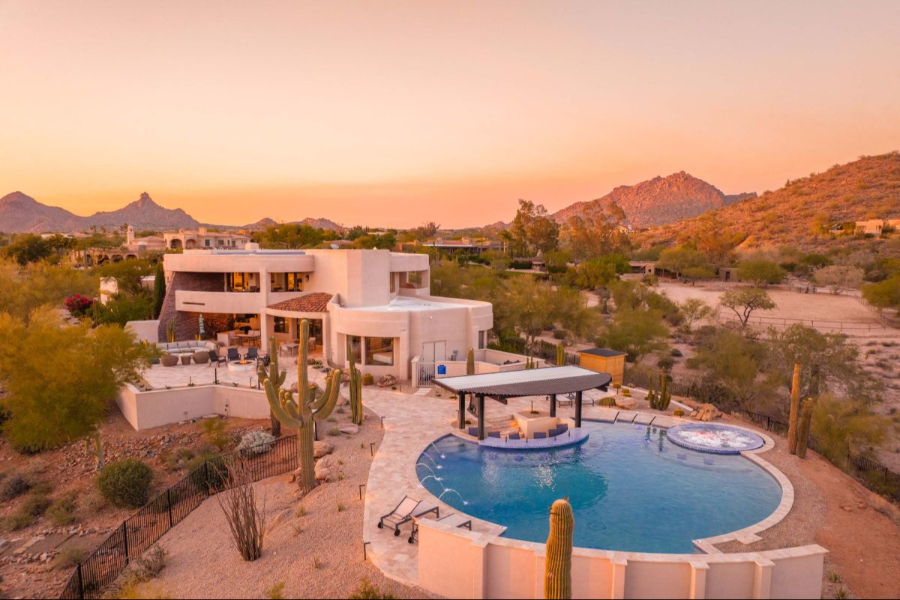 Luxury desert estate with pool, surrounded by cacti, nestled in Scottsdale's mountainous landscape at sunset.