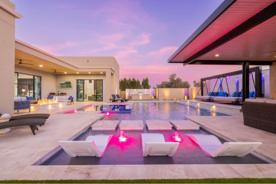 Luxurious Scottsdale estate featuring a modern pool with lounge chairs, fire pit, and ambient purple lighting at dusk.