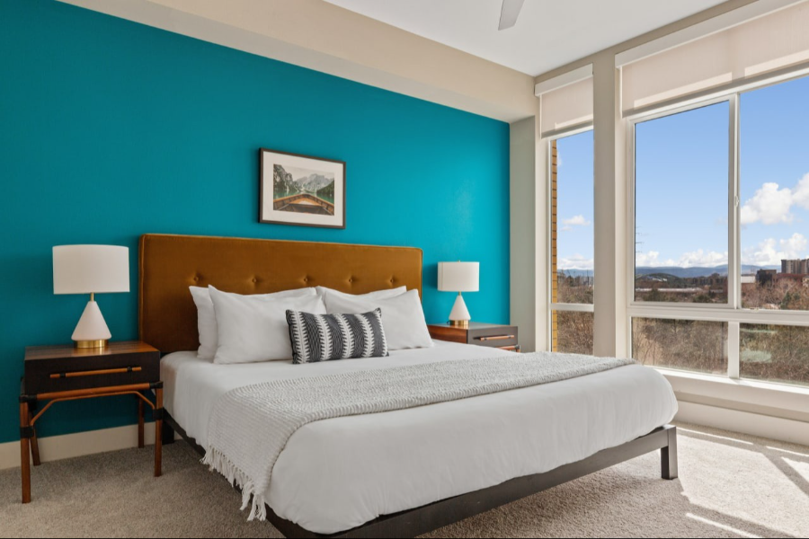Luxurious bedroom in Denver's Kasa Union Station, featuring a plush bed with teal accent wall and large window with a scenic view.