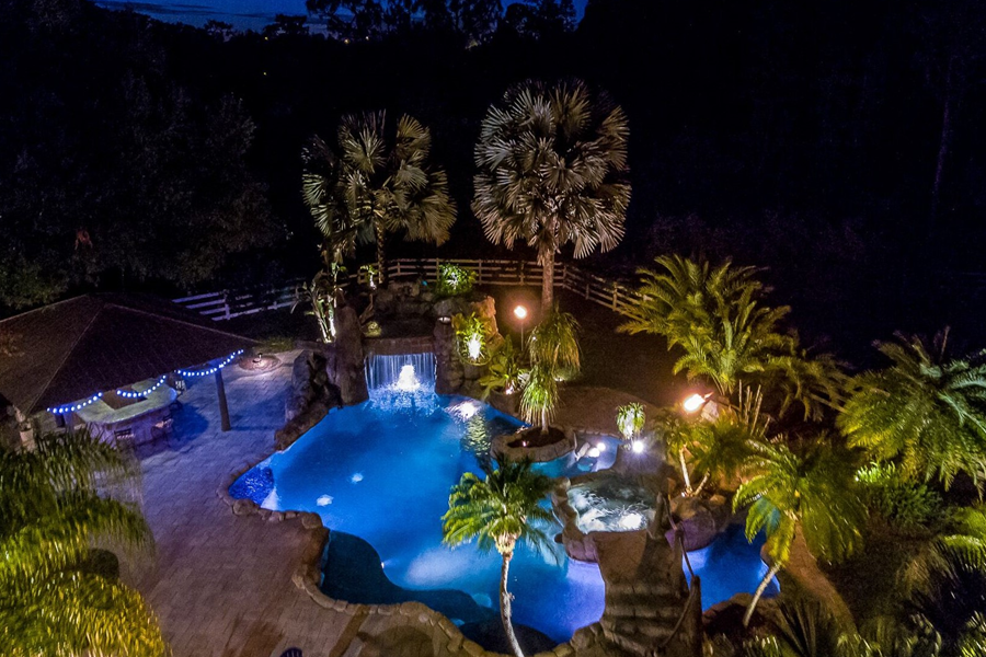 Tampa - Private Vacation Home - 6 Bedrooms / 4 Baths - 6 Beds + Sofa Sleeper Stunning night view of a luxury backyard pool with cascading waterfall and illuminated palm trees at a Tampa vacation home.