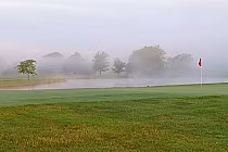Foggy golf course with a red flag on the green, trees, and a pond in the background at St. Clair Parkway, Ontario.