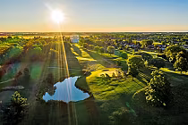 Scenic aerial view of Kingswell Glen Golf Course at sunrise, showcasing lush greenery, trees, and a small reflective pond.