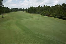 Lush green golf fairway with a hole flag at Sandpiper Bay, surrounded by trees and a small pond under a cloudy sky.
