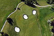 Aerial view of a golf course hole with three sand bunkers, surrounded by lush green fairways and trees.