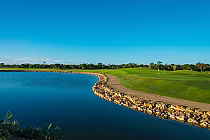 Stunning view of Dye Fore Golf Course featuring a clear lake, lush green fairways, and a bright blue sky at Casa de Campo.