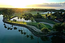 Sunset view of Casa de Campo golf course, lush greens, palm trees, and water features reflecting a golden sky.
