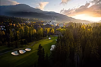 Aerial view of Chateau Whistler Golf Club at sunset, surrounded by lush forests and mountains, highlighted by a warm glow.