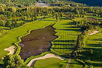 Aerial view of Big Sky Golf Club's lush fairways and tranquil lake, framed by dense woodland near Whistler, Mount Currie.