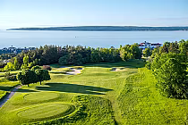 Scenic view of Crooked Tree Golf Club with lush fairways, trees, and Lake Michigan in the background on a sunny day.