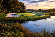 Scenic golf course with lush greens, sand bunkers, and pond reflecting sunset, set against a backdrop of trees at The Highlands.