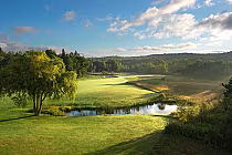 Scenic view of The Moor Course at The Highlands, featuring lush greenery, a pond, and a clear blue sky.