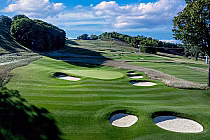 Doon Brae Course at The Highlands, MI, features lush greens, sand traps, and rolling hills under a vivid blue sky.